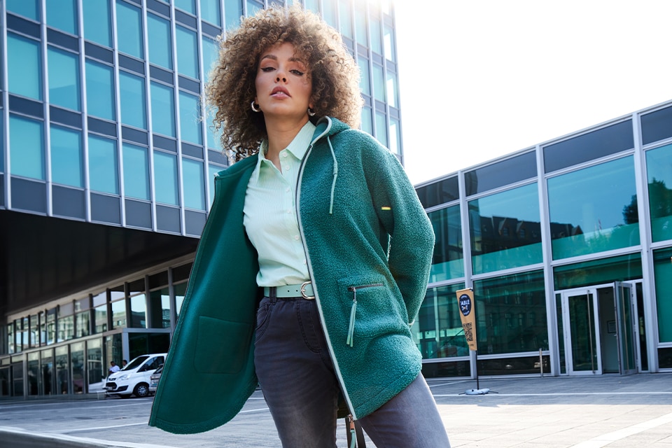 The model poses in a green teddy jacket and a shirt with a print