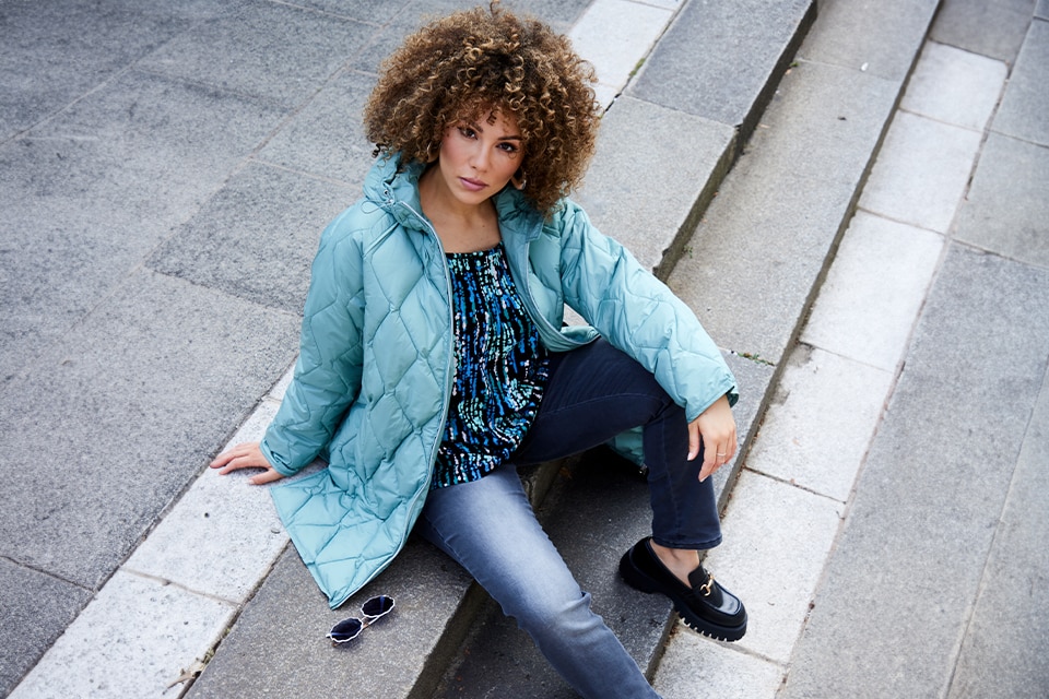 The model wears a green quilted jacket with a patterned blouse 