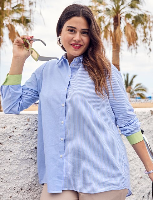 The model poses sitting in a colorful blouse and wears a pair of jeans
