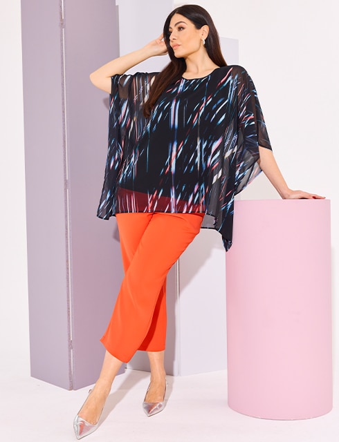 The model wears a blue blouse with stripes and orange trousers

