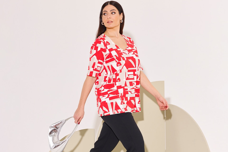 The model wears a red nd white patterned shirt and black trousers

