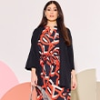 The model wears a black cardigan and a dress with the colors orange and blue

