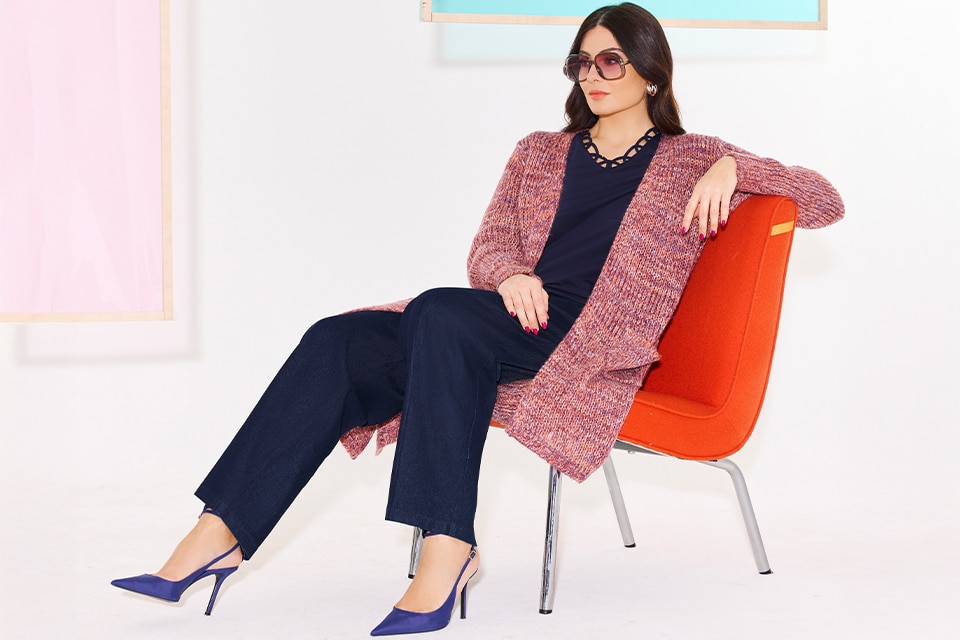 The model wears a red cardigan and a blue shirt and pants