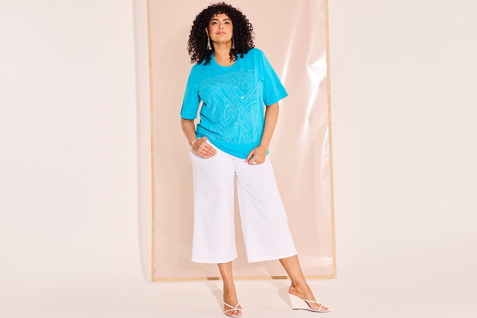 The model is wearing a turquoise shirt and white pants.