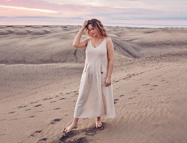 The model walks in the desert and wears a beige dress 