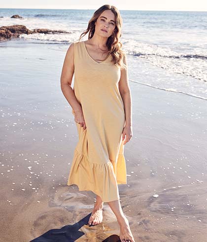 The model stands in front of the sea while she is wearing a yellow dress 
