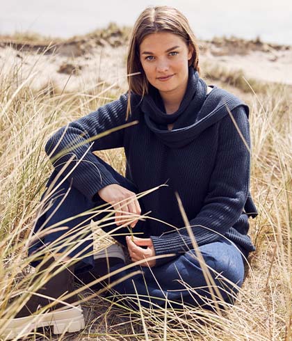 The model sits in the dunes in a blue sweater