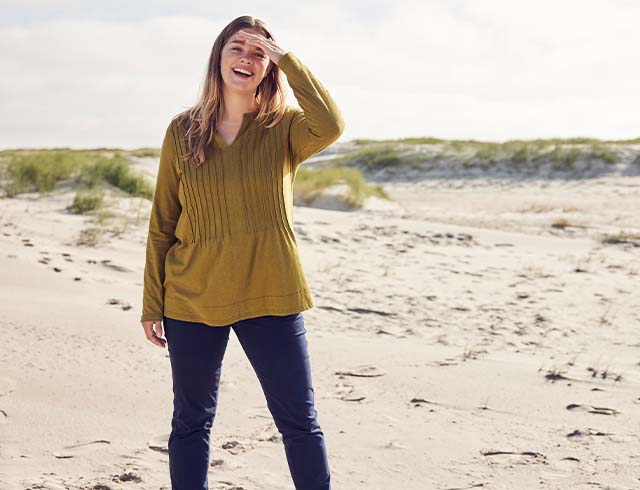 The model stands on the sand and wears a green t-shirt

