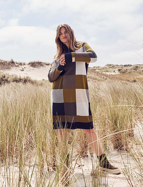 The model stands in the dunes and wears a plaid knit dress 

