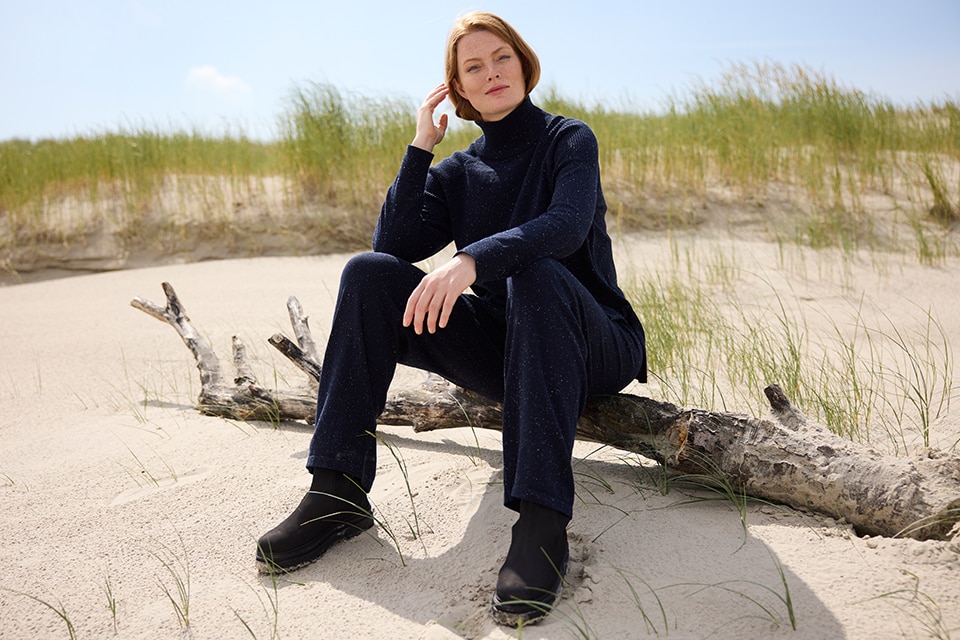 The model poses sitting in a black sweater with matching pants 