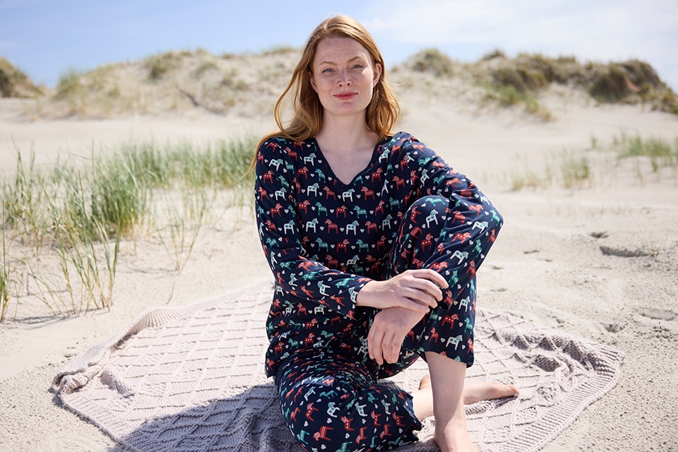 The model sits in sand and wears patterned pyjamas 