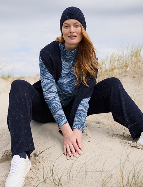 The model poses in a pink skirt and white jumper in a field 