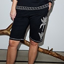 The model poses on a lilla couch wearing a combination of a white shirt and shorts