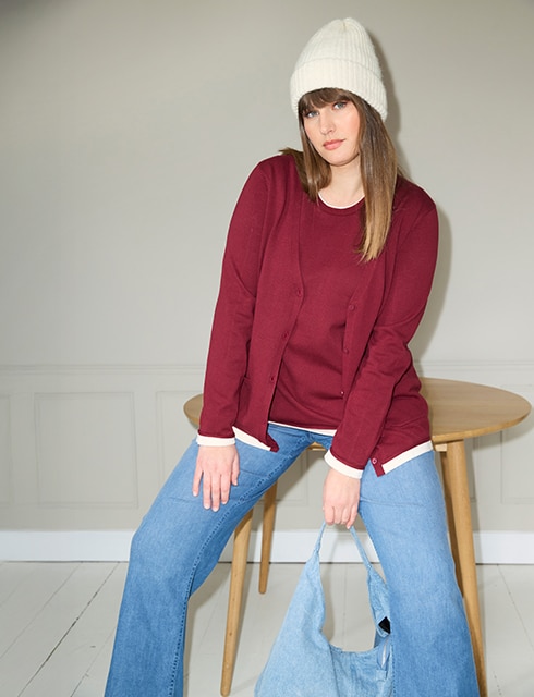 The model poses in a pink skirt and white jumper in a field 