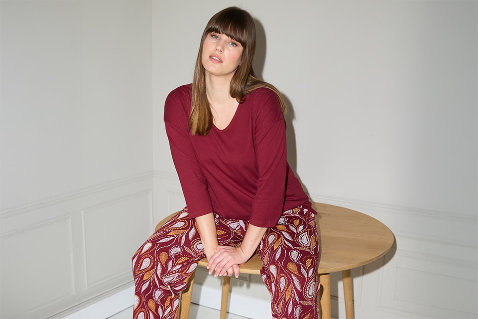 The model wears a burgundy pajama set with a print on the pants.

