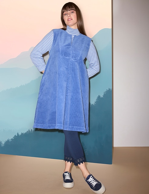 The model poses in a pink skirt and white jumper in a field 