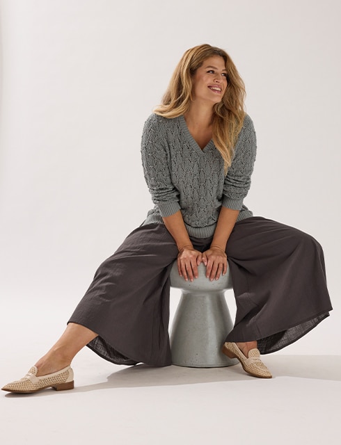 The model poses in a pink skirt and white jumper in a field 