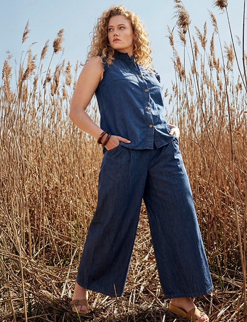 The model poses in a pink skirt and white jumper in a field 