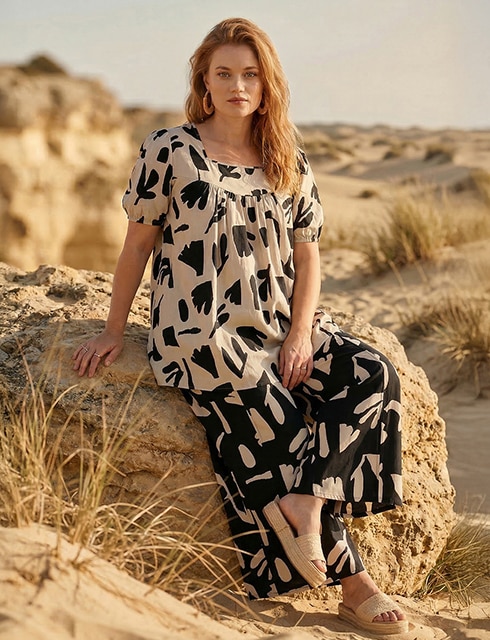 The model poses in a pink skirt and white jumper in a field 