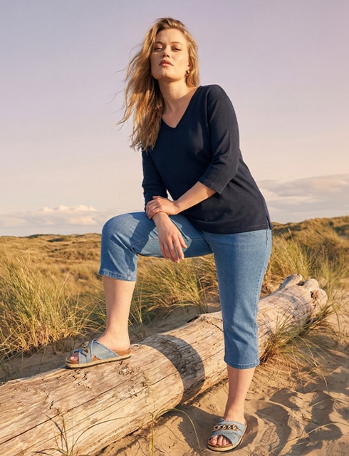 The model poses in a pink skirt and white jumper in a field 