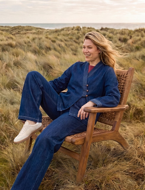 The model poses in a pink skirt and white jumper in a field 