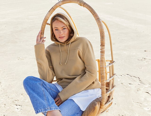 Frau sitzend auf einem Holzstuhl in beigem Pullover