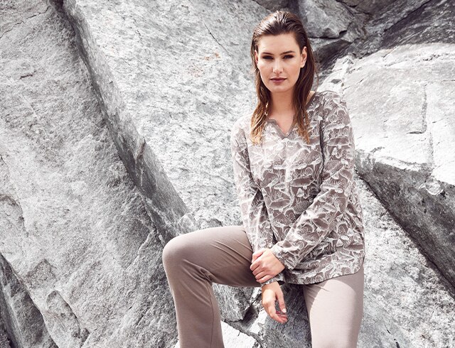 Woman in brown and white patterned top sits on a rock