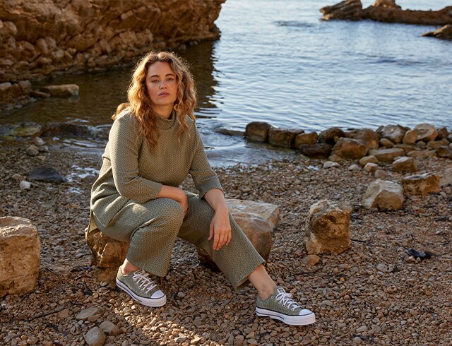 Woman in a green sweatshirt sits on some rocks next to water