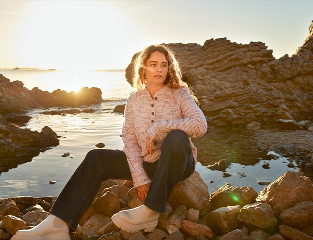 Woman in a sweatshirt sits on some rocks