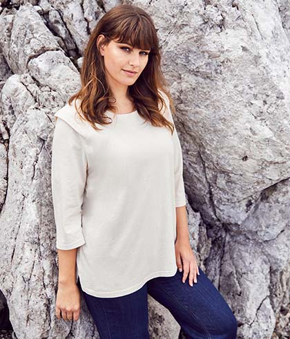 Model in white top leans against rock face 