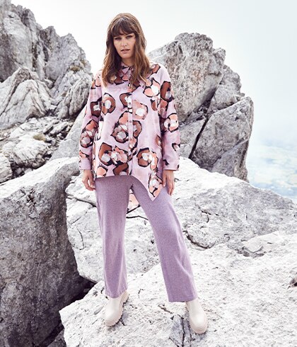 Woman with a purple blouse and trousers stands on a rock