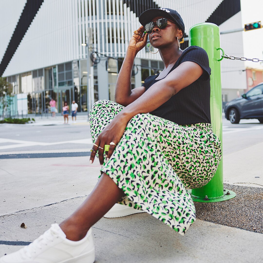 Dark-skinned model leaning against a green pillar wearing a black t-shirt and a green skirt