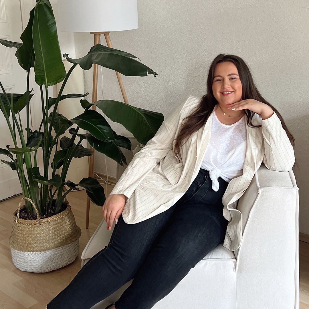 Woman wearing a striped blazer and dark jeans while sitting on a white armchair