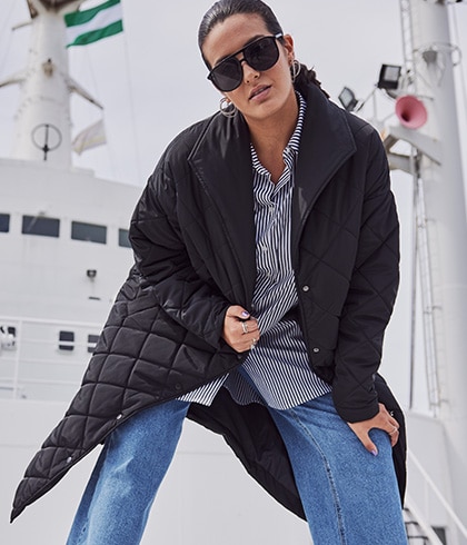 Woman standing on a ship is wearing a black coat and a jeans.