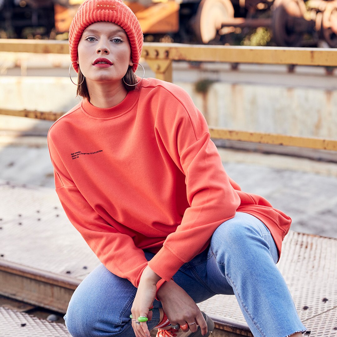Model trägt einen orangen sweater und eine orange Wollmütze