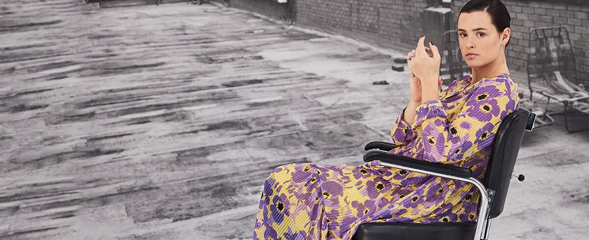 Model wearing a dress with flower print is sitting on a chair