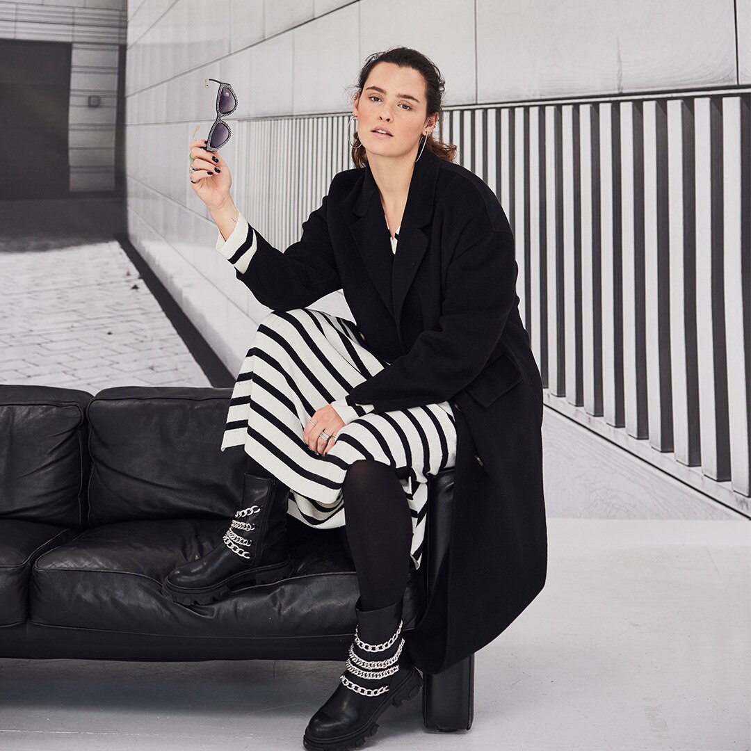 Model wearing a black coat is posing on a black sofa