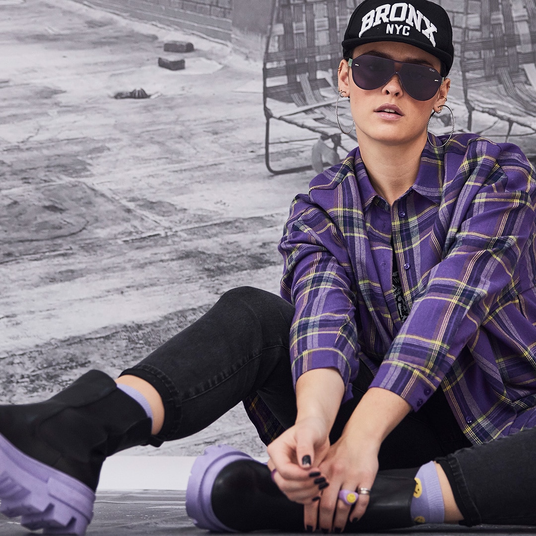 Model is sitting on the floor wearing sunglasses and a purple shirt