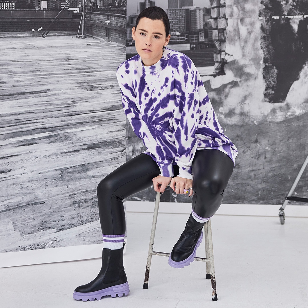 Model is sitting on a chair wearing a white and purple colored sweater