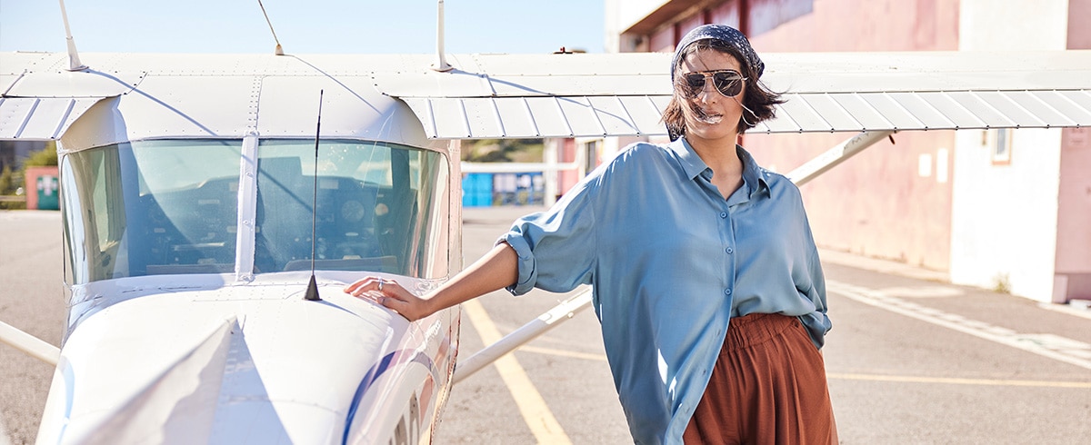 Model posing next to an airplane wearing a blue blouse