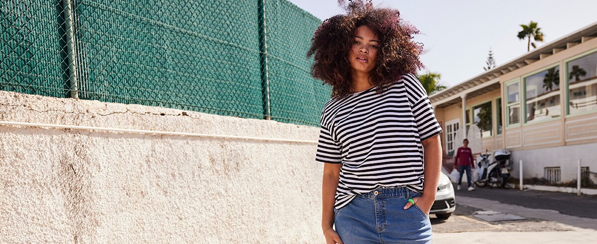 A Model is wearing a shirt with stripes while posing next to a wall 