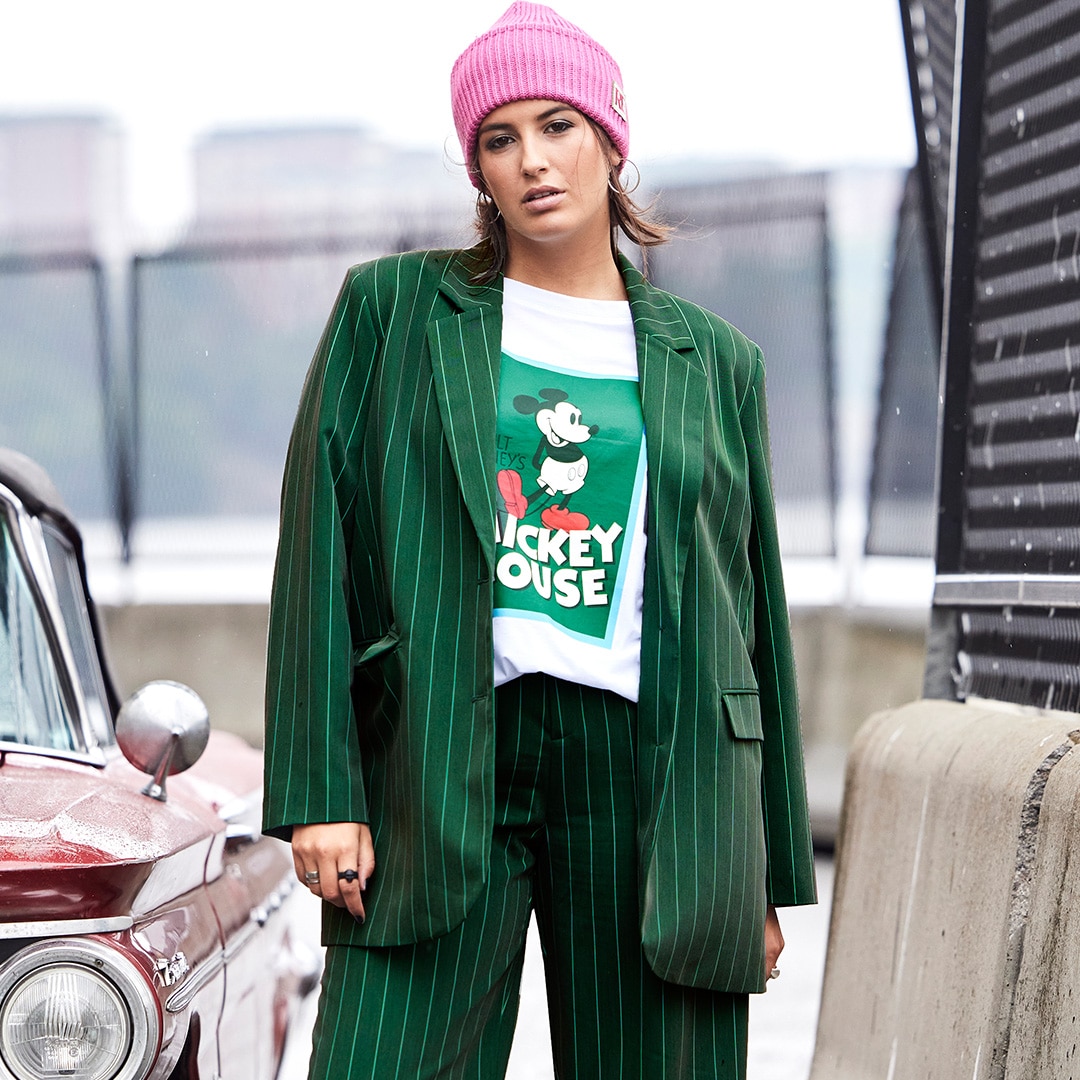 Model is standing beside a car in a pink beanie and a green blazer 