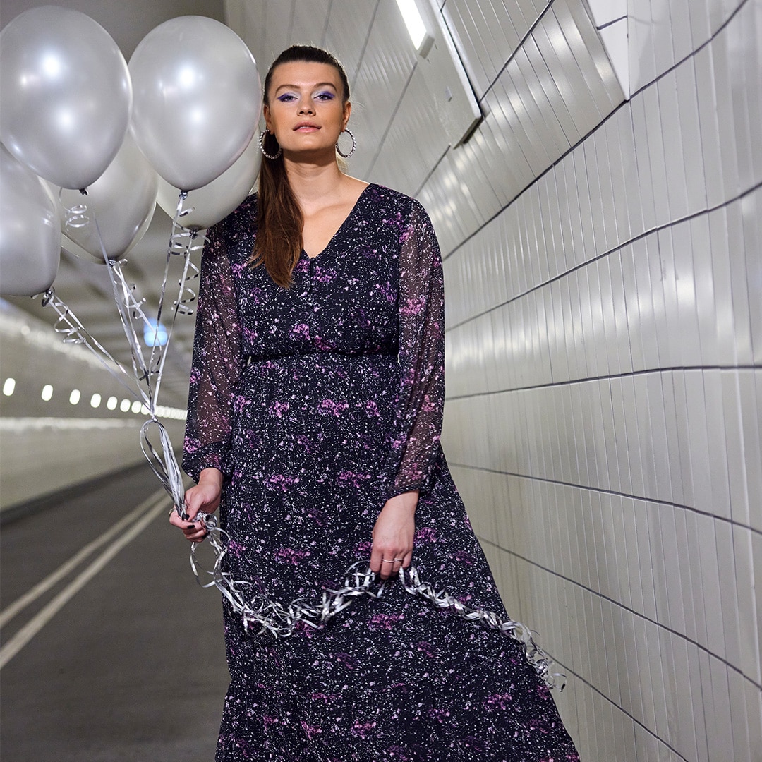 Woman is wearin a galaxy printed dress while standing in a tunnel