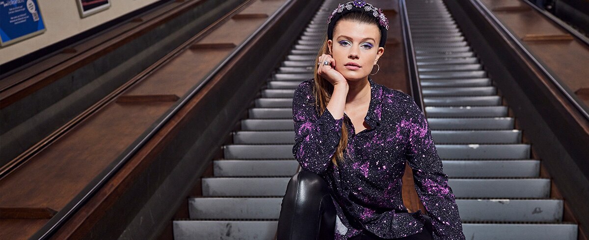 A model is wearing a galaxy printed blouson while sitting beside an escalator
