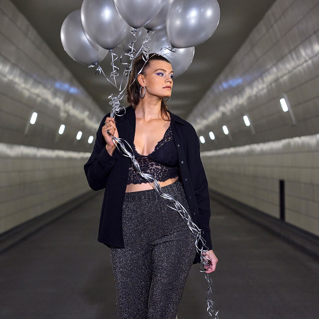 Model is wearing black shiny clothes and is holding black baloons