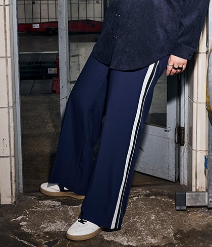 The model is wearing a black shirt and burgundy trousers with a diamond-shaped pattern.