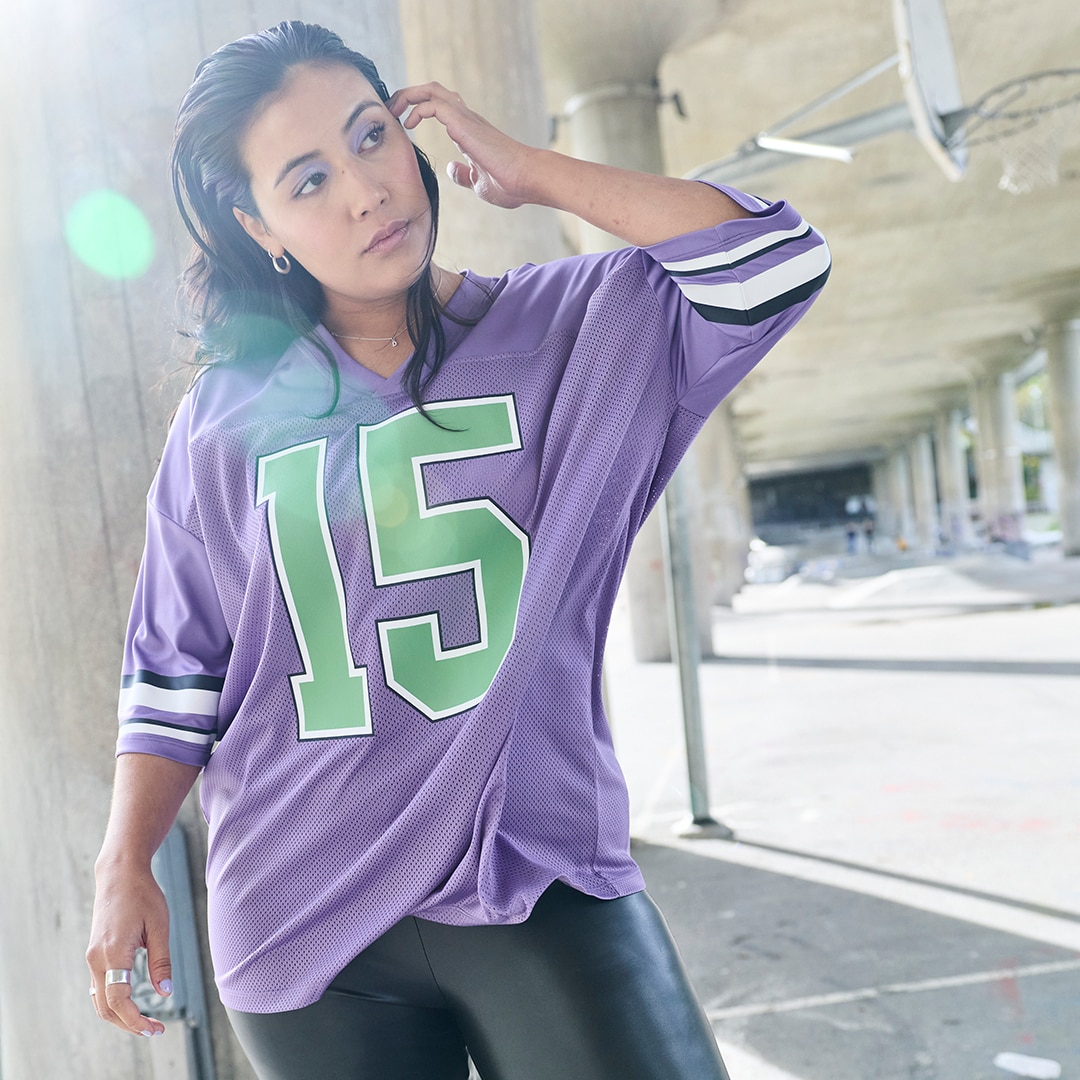The model is wearing a purple football shirt with green numbers on the front.
