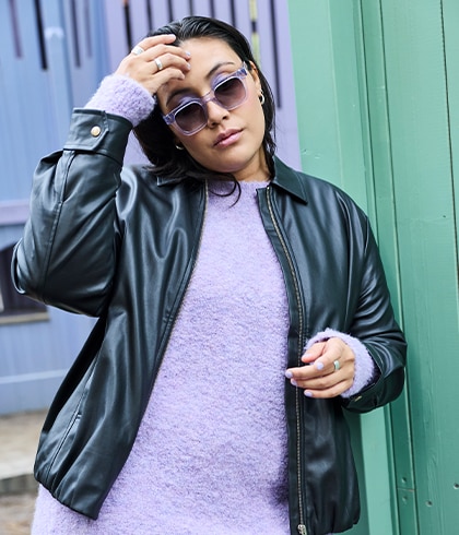 The model is wearing a black leather jacket over a purple jumper.