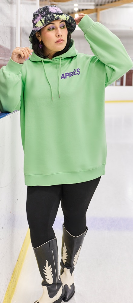 The model is wearing a neon green sweatshirt with leggings and cowboy boots.