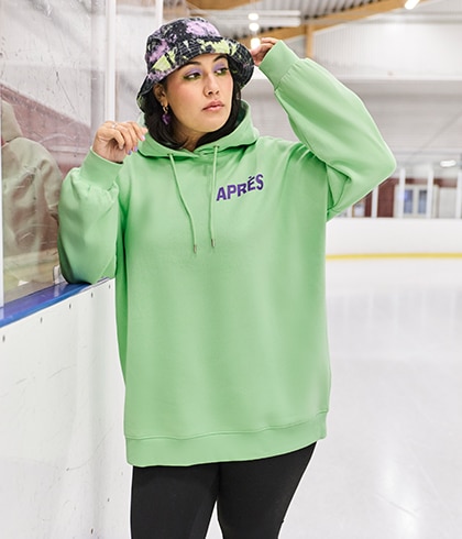 The model is wearing a neon green sweatshirt with leggings and cowboy boots.